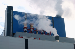 Industrial cooling towers releasing visible water vapor beside a large commercial building.