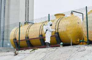 Technician applying chemical treatment near industrial storage tanks as part of a water disinfection program.