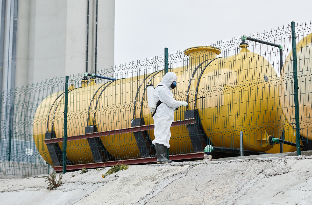Technician applying chemical treatment near industrial storage tanks as part of a water disinfection program.