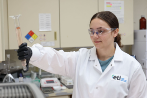 Laboratory technician wearing an ETI lab coat examines a liquid sample in glassware