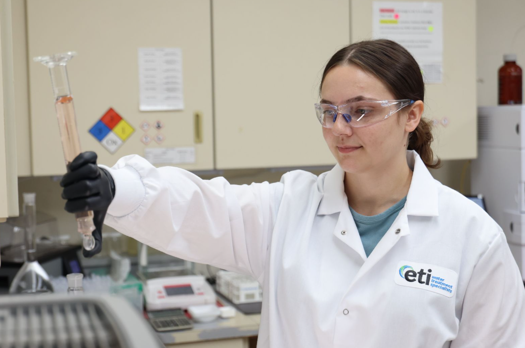 Laboratory technician wearing an ETI lab coat examines a liquid sample in glassware